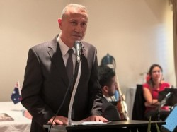 A person in a suit standing at a podium with a microphone

Description automatically generated