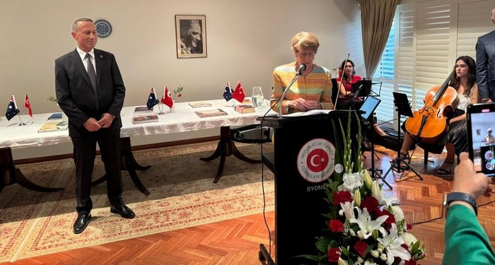 A person standing at a podium with a person standing behind a table

Description automatically generated