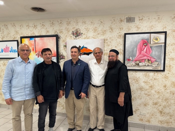 A group of men standing in a room with paintings on the wall

Description automatically generated