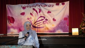 A person in a headscarf speaking into a microphone

Description automatically generated