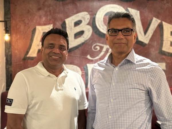 Two men standing in front of a sign
Description automatically generated
