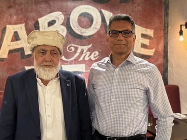 Two men standing in front of a sign
Description automatically generated