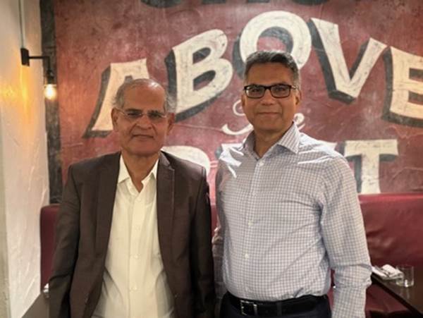 Two men standing in front of a sign
Description automatically generated