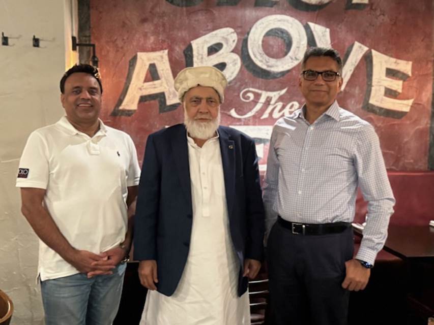 A group of men standing in front of a sign
Description automatically generated