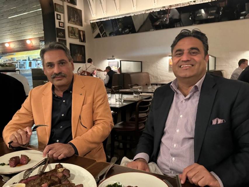 Two men sitting at a table with food
Description automatically generated