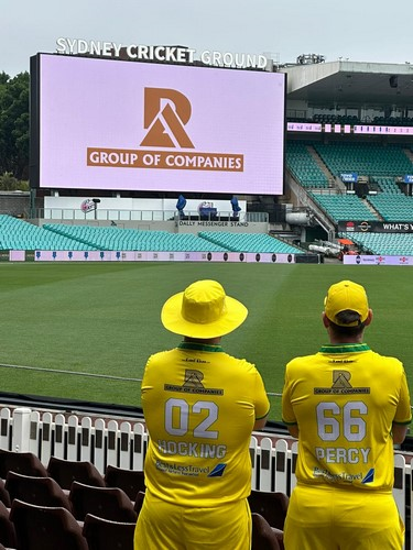 Two people in yellow shirts and hats looking at a large screen
Description automatically generated