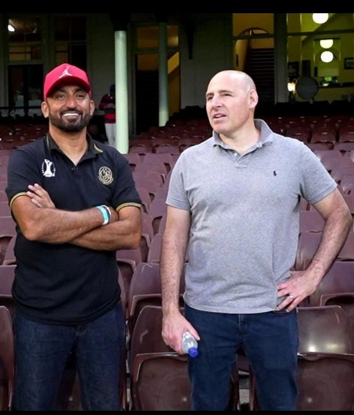 Two men standing in a stadium
Description automatically generated