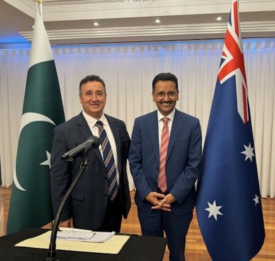 Two men standing in front of a microphone and flags
Description automatically generated