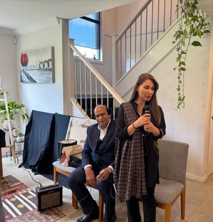 A person holding a microphone next to a person sitting on a chair
Description automatically generated