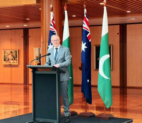 A person standing at a podium with a microphone and flags
Description automatically generated