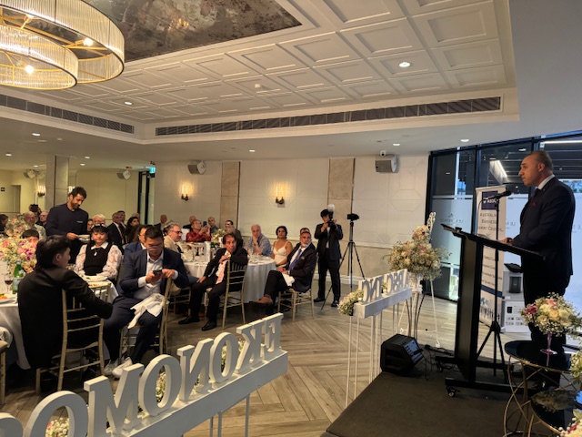 A person standing in front of a podium with a crowd of people
Description automatically generated