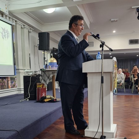 A person standing at a podium speaking into microphones

Description automatically generated