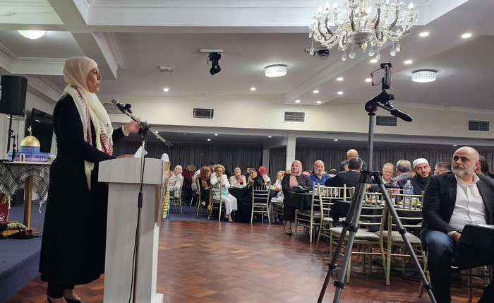 A person standing at a podium with a microphone in front of a crowd of people

Description automatically generated