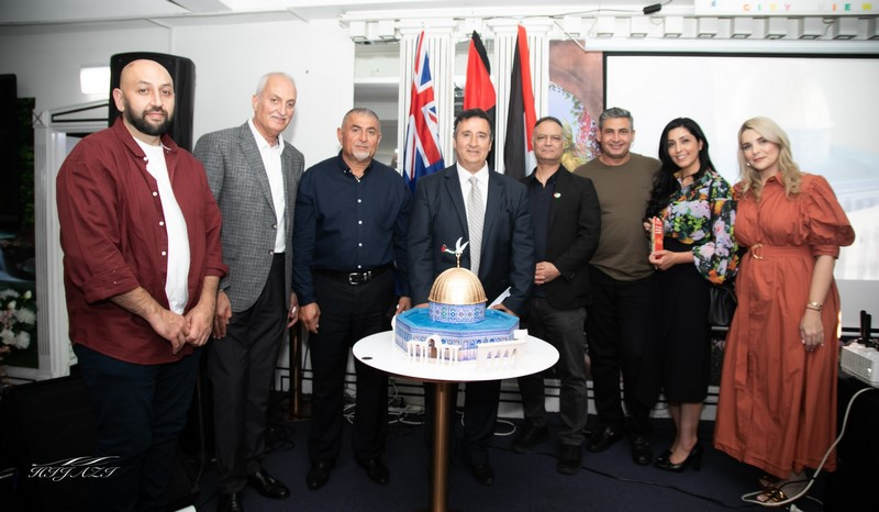 A group of people standing in front of a cake

Description automatically generated