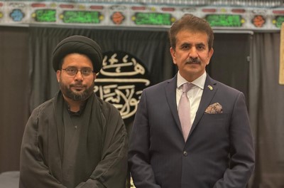 Two men standing together in front of a sign
Description automatically generated