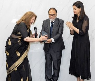 A person in a suit and person in black dress receiving an award
Description automatically generated