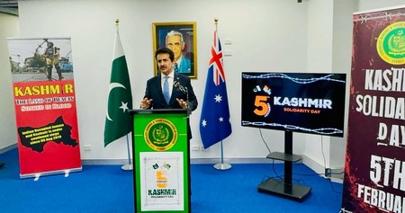 A person standing at a podium with flags in the background
Description automatically generated