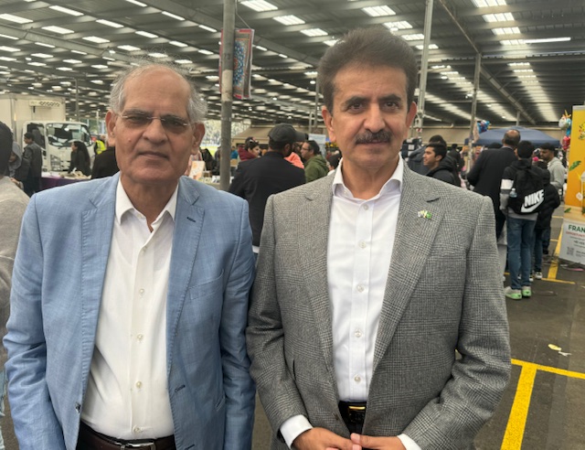 Two men standing together in a building
Description automatically generated