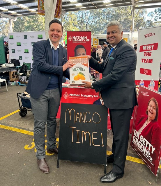 Two men standing next to a sign
Description automatically generated