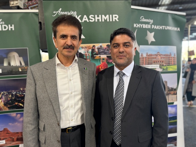 Two men standing together in front of a sign
Description automatically generated