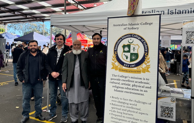 A group of men standing in front of a sign
Description automatically generated