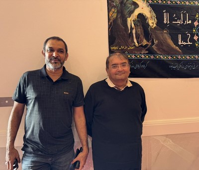 A couple of men standing in front of a poster
Description automatically generated