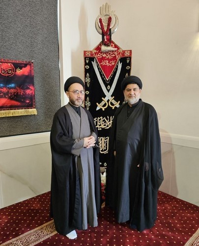 Two men standing in front of a large black and red cloth
Description automatically generated