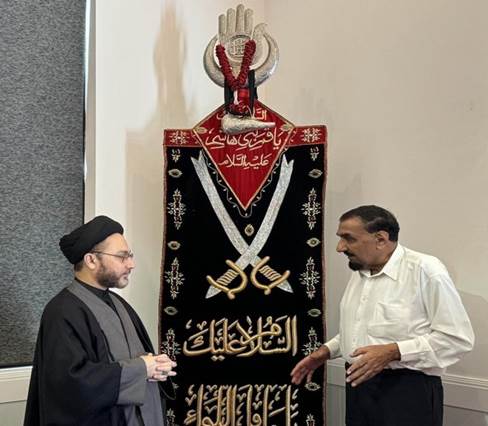 Two men standing next to a large black and red banner
Description automatically generated