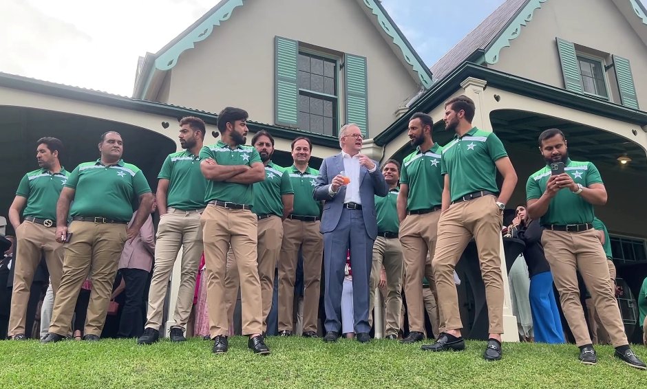 A group of men in green shirts standing in front of a house

Description automatically generated