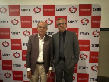 Two men standing in front of a wall with red and white signs
Description automatically generated