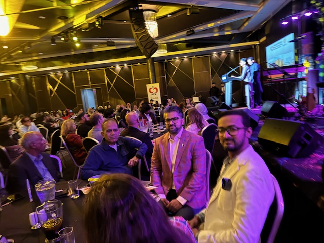 A group of people sitting in a room with a stage and a microphone
Description automatically generated