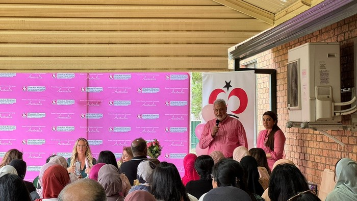 A person in pink shirt speaking into a microphone

Description automatically generated